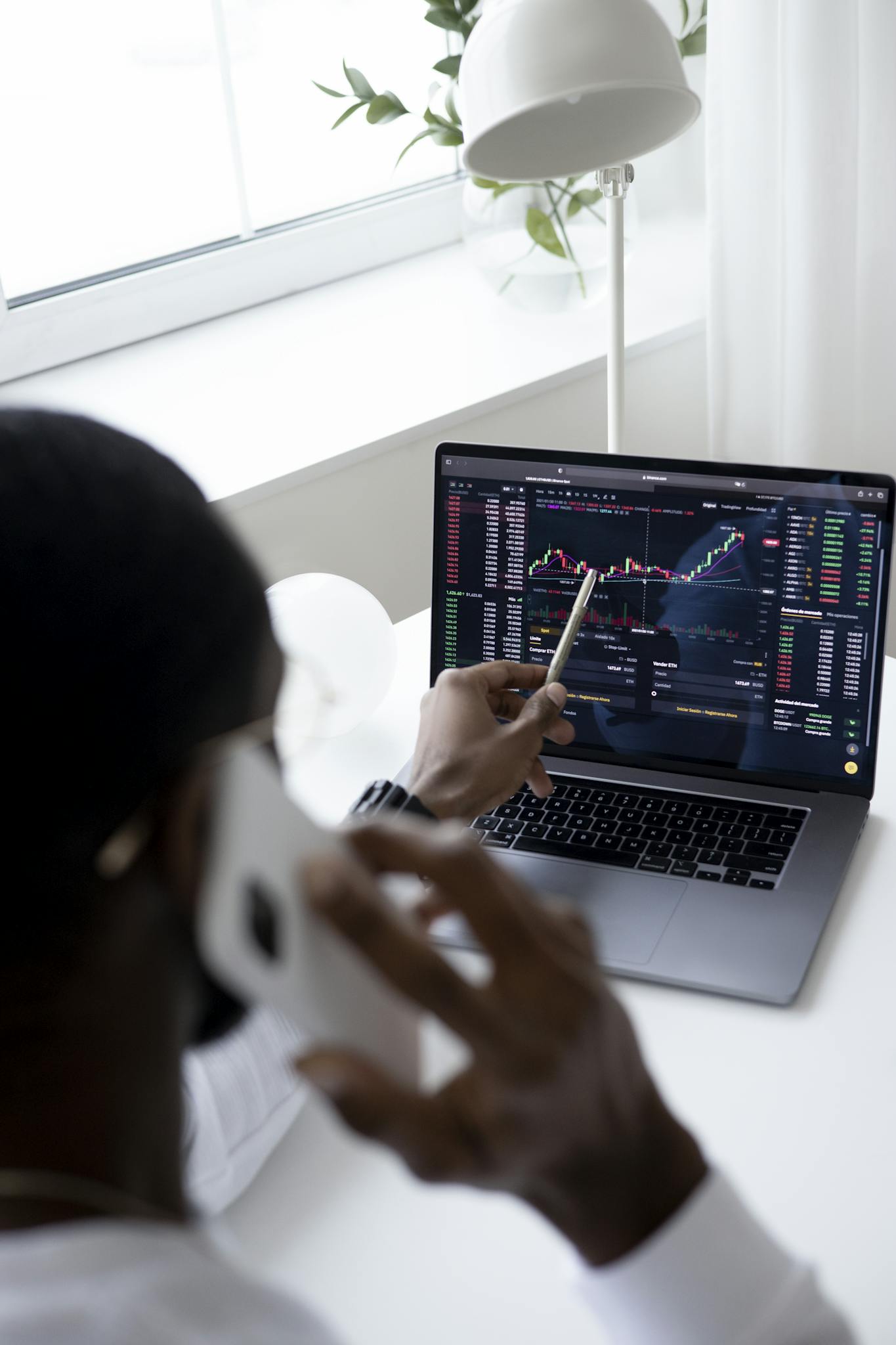 Our Mission A businessman using a smartphone while analyzing stock market graphs on a laptop indoors.